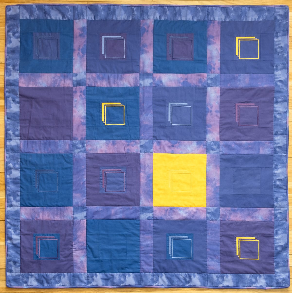 a square blocked quilt in purples and blues with yellow accents